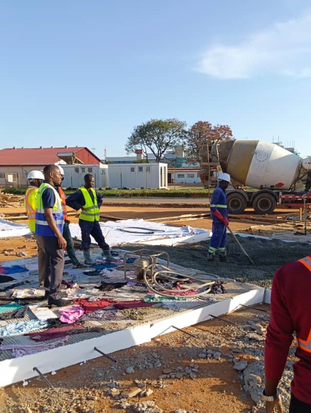Workers placing concrete over reinforcement on a large paved site