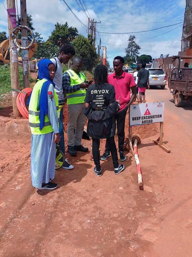 People standing beside a deep-excavation warning sign on an urban street